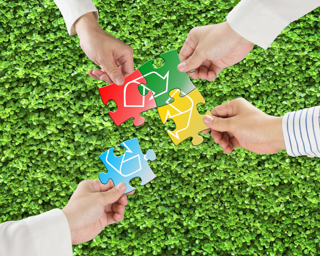 Hands hold puzzles with recycle symbol in fresh meadow background